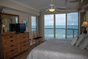 A bedroom with a large bed, a dresser, a television, and a view of the ocean through a balcony.