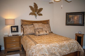 Une chambre à coucher avec un lit en bois, une table de chevet avec une lampe, un tableau encadré au mur et une horloge sur la table de chevet.