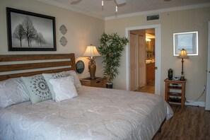 Une chambre à coucher avec un grand lit, deux tables de chevet avec des lampes, une plante en pot et un tableau encadré au mur.