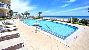 A rectangular pool with a diving board, surrounded by lounge chairs and a palm tree.