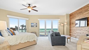 A bedroom with a bed, a gray armchair, a wooden cabinet, and a large window overlooking the ocean.
