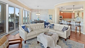 A spacious living room with a sectional sofa, a coffee table, and a view of the kitchen through an open door.