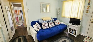 A room with a blue sofa, a television on a small stand, a mirror on the wall, and a door leading to another room.