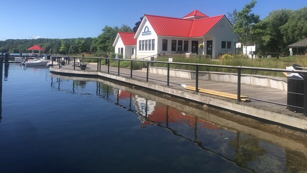 A waterfront property with a red-roofed building, a dock with a boat, and a calm water body reflecting the structure. - Quaint Northport cabin a short distance from the village. A/C. (Northport)