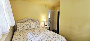 A bedroom with a bed, a nightstand, a lamp, and a door leading to another room.