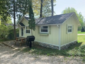 A small, single-story cabin with a stone foundation, a picnic table, and a grill outside.