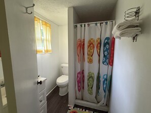 A bathroom with a toilet, a shower curtain with flip-flop patterns, and a towel rack. - Quaint Northport cabin with a short walking distance to village. (Northport)