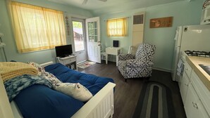 A compact room with a bed, a desk, a chair, a small kitchenette, and a ceiling fan. - Quaint Northport cabin a short distance from the village. A/C. (Northport)