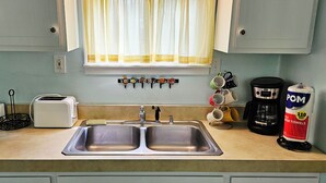 A kitchen with a double sink, a toaster, a coffee maker, and a bag of POM super towels. - Quaint Northport cabin a short distance from the village. A/C. (Northport)