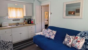 A compact room with a kitchenette, a blue sofa with patterned cushions, a mirror, and a door leading to another room. - Quaint Northport cabin a short distance from the village. A/C. (Northport)