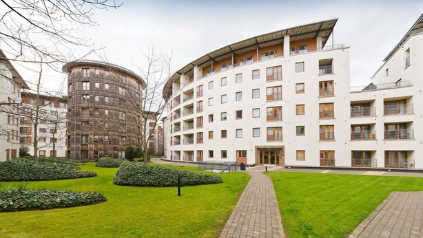 Un immeuble d’appartements moderne, doté de plusieurs étages, d’une cour intérieure avec un chemin piétonnier et d’un espace verdoyant tout autour.
