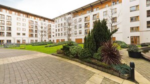 Un immeuble d’appartements moderne, doté de plusieurs étages, d’une cour pavée et de jardins aménagés.