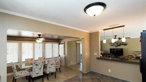 A spacious dining area with a high ceiling fan, a large window with blinds, and a modern kitchen with a built-in refrigerator and pendant lights. - The Boat House (Cape Coral)