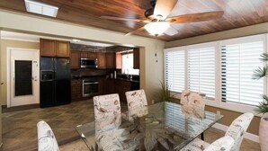 A modern kitchen with dark cabinets, a black refrigerator, and a microwave. There is a dining area with a glass table and chairs with a bird pattern. - The Boat House (Cape Coral)
