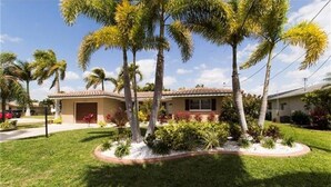 A single-story house with a tiled roof, surrounded by a well-maintained lawn and palm trees. - The Boat House (Cape Coral)