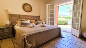 A bedroom with a bed, bedside tables, a mirror, and a view through an open door to a garden. - Villa Lucendiluna. 10 pers, piscine, 5 min plage en voiture (Zonza)