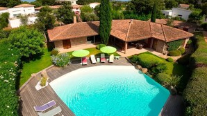 A large swimming pool with a wooden deck, surrounded by lounge chairs and umbrellas, set in a lush garden with a view of neighboring houses. - Villa Lucendiluna. 10 pers, piscine, 5 min plage en voiture (Zonza)