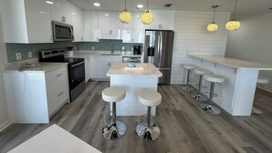 Una cocina moderna con muebles blancos, electrodomésticos de acero inoxidable y una isla central con taburetes.