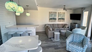 Un salón moderno con sofá, un sillón estampado, una mesa de centro redonda y una zona de bar con taburetes.