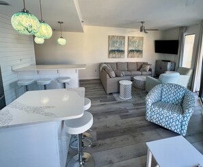 Ein modernes Wohnzimmer mit einer Couch, einem gemusterten Sessel, einem runden Couchtisch und einer Bar mit Hockern.