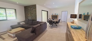 Un salon moderne comprenant un canapé d’angle, une table à manger avec des chaises, une table basse en bois et un mur d’accent en pierre.