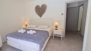 A hotel room with a bed, two bedside tables, a heart-shaped wall decoration, and a door. - Villa Tinuta. 8 pers, piscine chauffée, 5 min plage en voiture (SAINTE LUCIE DE PORTO VECCHIO)