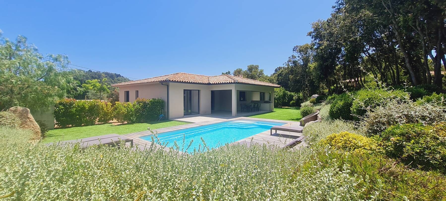 A modern house with a swimming pool, surrounded by lush greenery and a clear blue sky.