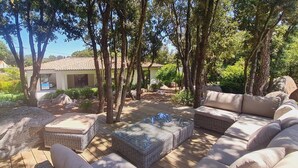 A patio area with wicker furniture, a stone bench, and a view of a house with a tiled roof. - Villa Tinuta. 8 pers, piscine chauffée, 5 min plage en voiture (SAINTE LUCIE DE PORTO VECCHIO)