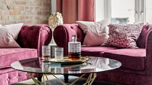A room with a plush red sofa, a glass coffee table, and a decorative bottle on a tray.