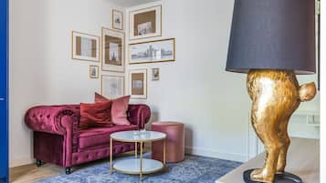 A living room with a red velvet sofa, a small round table, a gold lamp, and framed pictures on the wall.