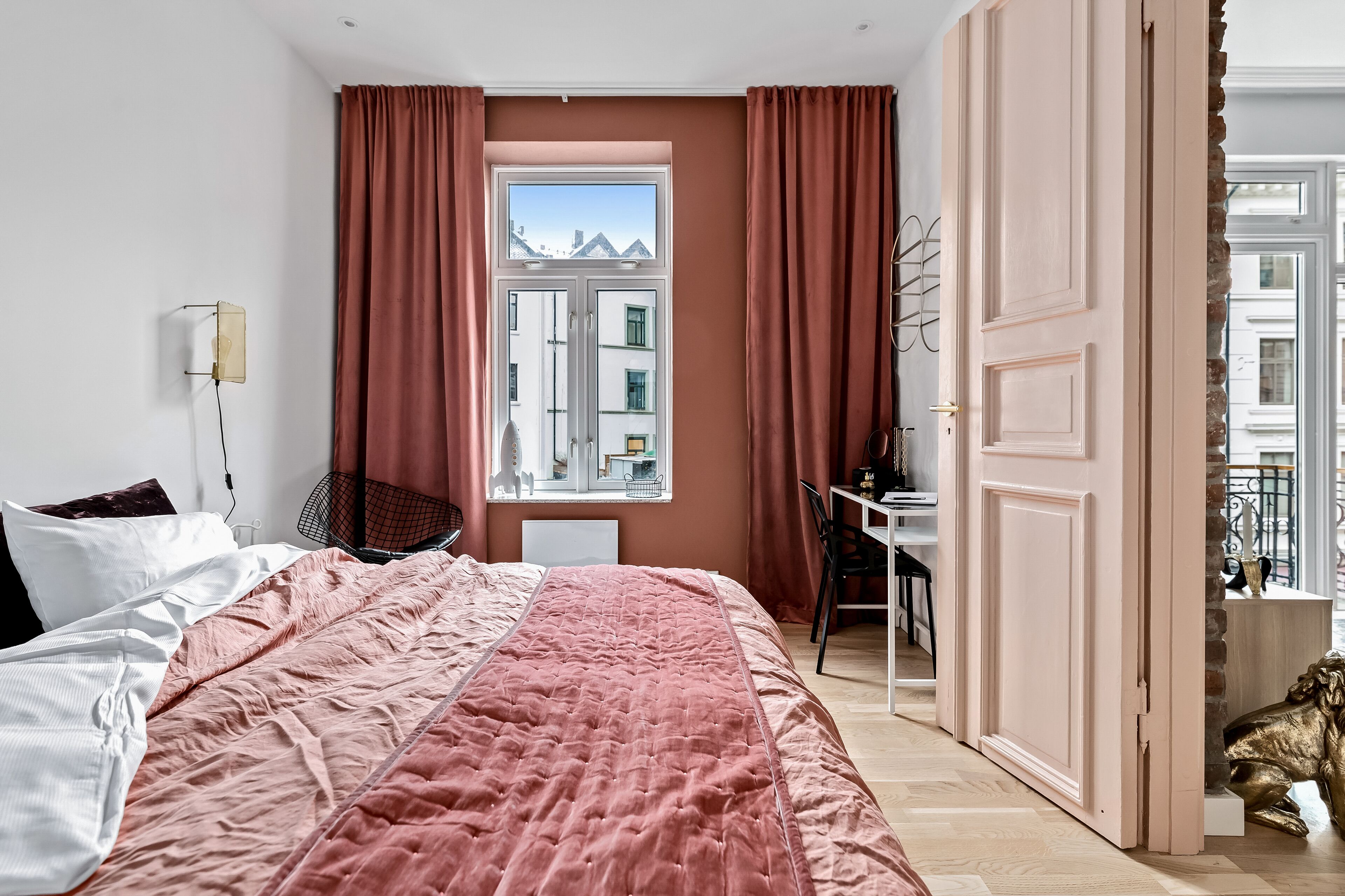 Un dormitorio con una cama grande, un escritorio y vistas a edificios a través de una ventana.