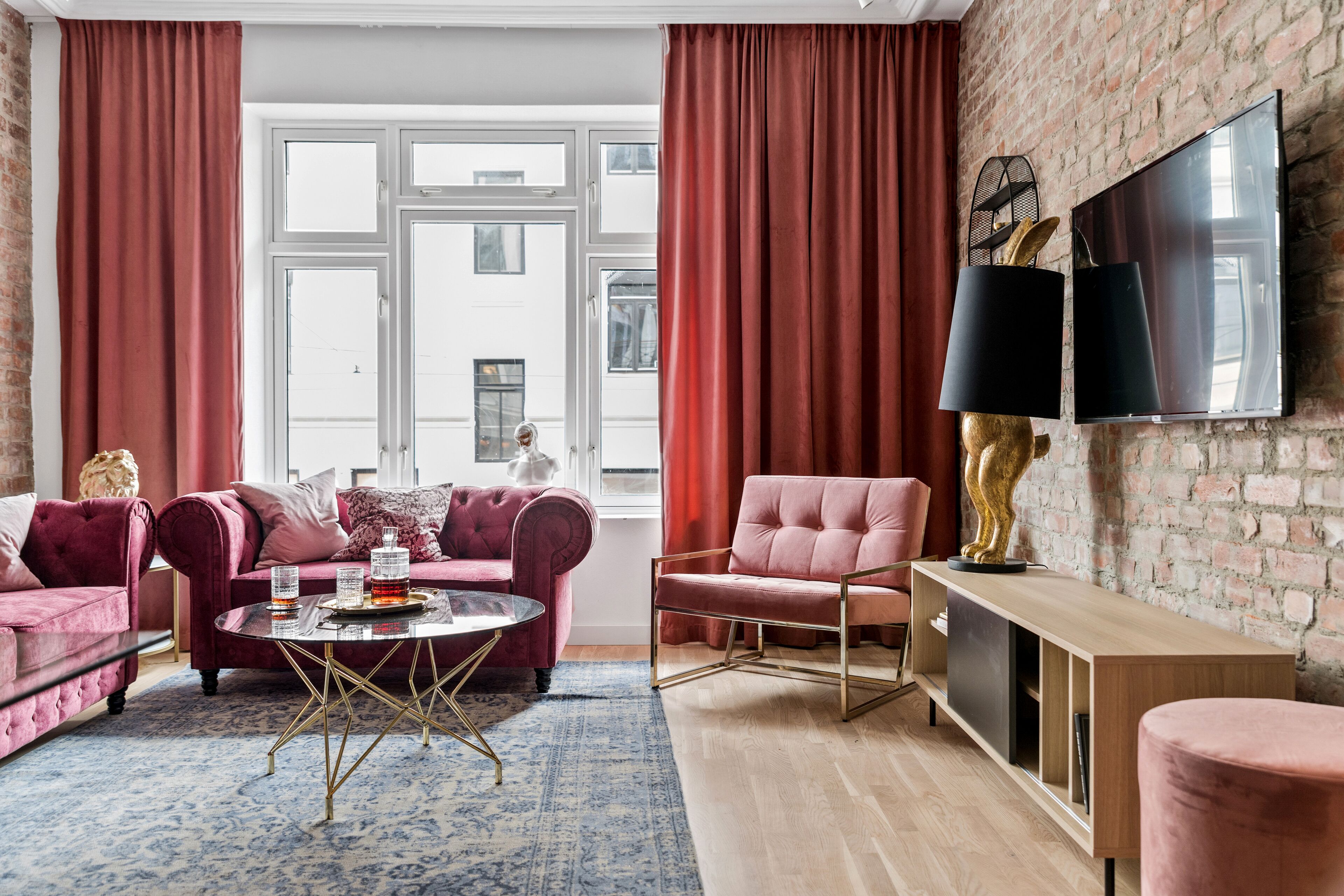 A modern living room with a brick wall, red curtains, a large TV, and plush seating.