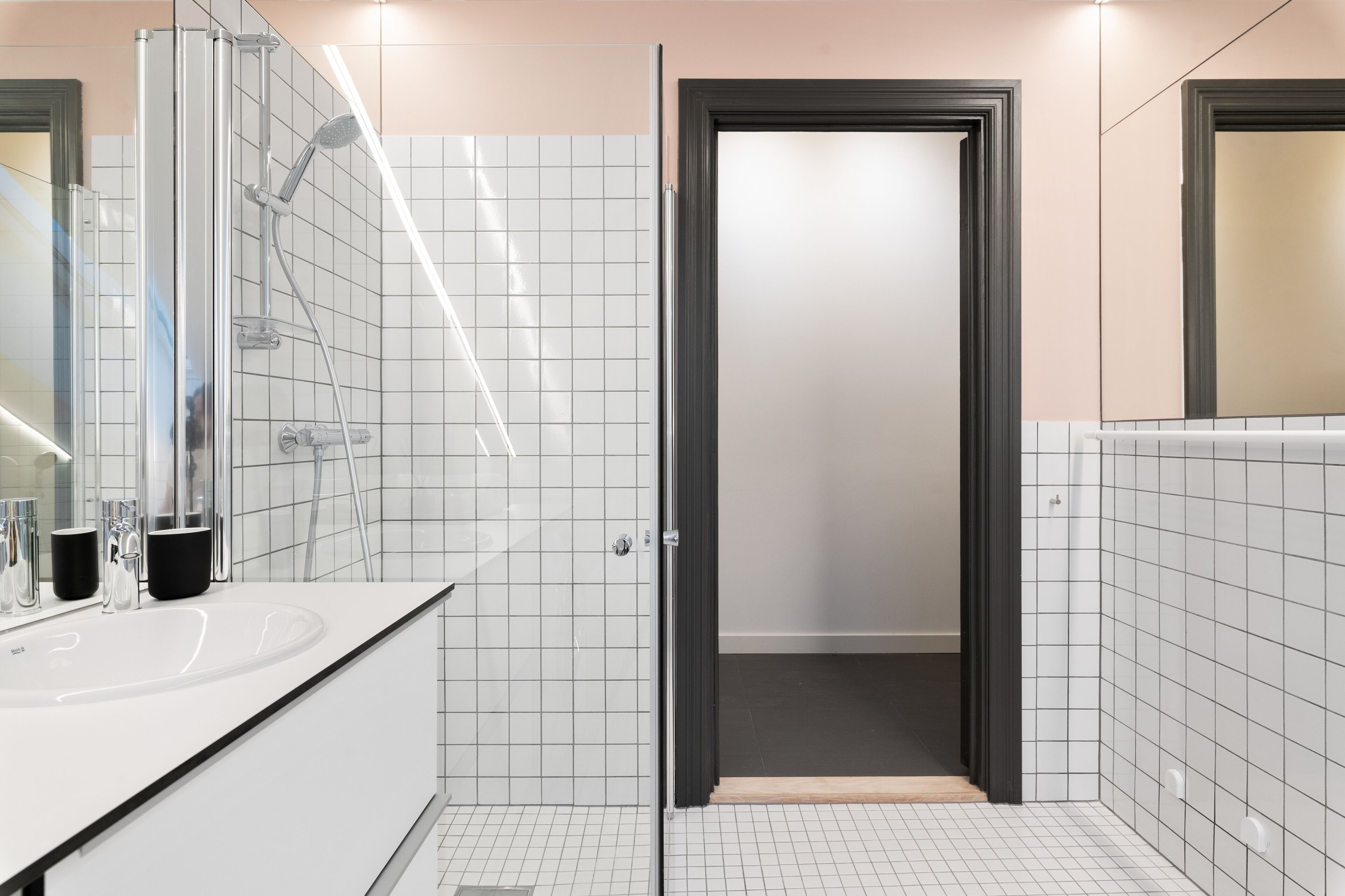 Een moderne badkamer met een wit wastafel, een zwarte beker en een douchecabine van glas.