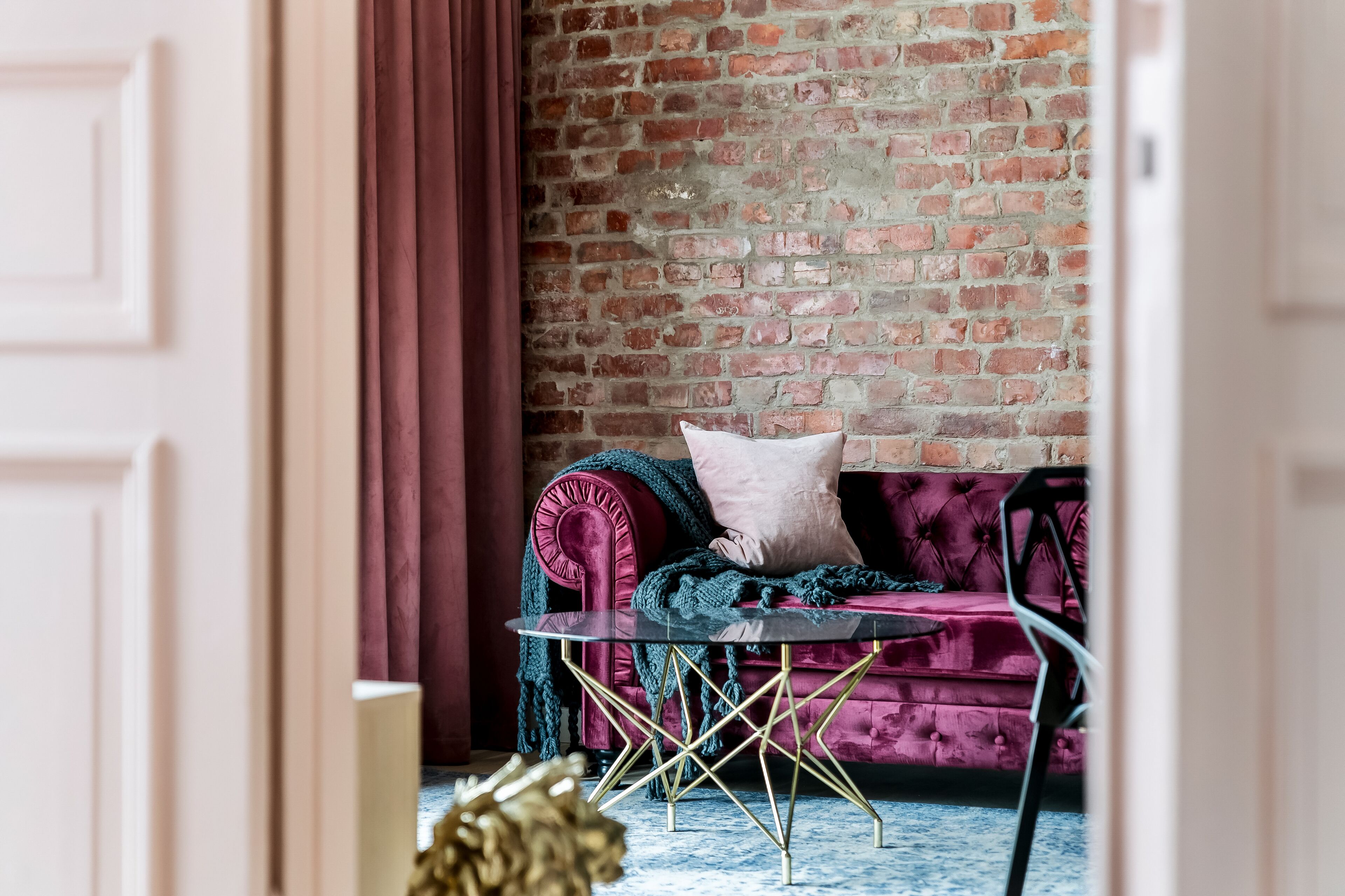 A room with a brick wall, a red velvet sofa with a glass table, and a red curtain.