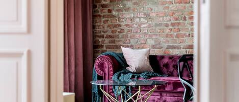 Una habitación con pared de ladrillo, un sofá de terciopelo rojo y una mesa de vidrio, además de una cortina roja.