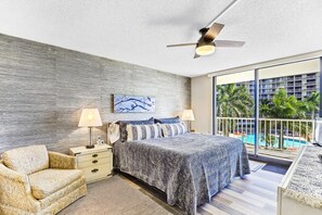Une chambre d’hôtel moderne avec un grand lit, deux lampes de chevet, un ventilateur de plafond et une vue sur une piscine.