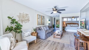 A modern living room with a sofa, armchair, coffee table, and a dining area with a bar. - Hale Ono Loa 106 - Relax Steps Away from the Ocean (Lahaina)