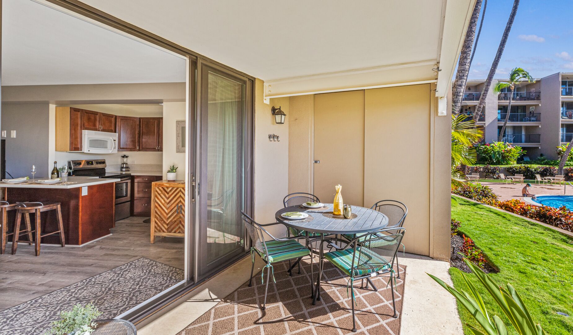 A modern kitchen with a central island, a dining area with a table and chairs, and a view of a swimming pool and greenery.