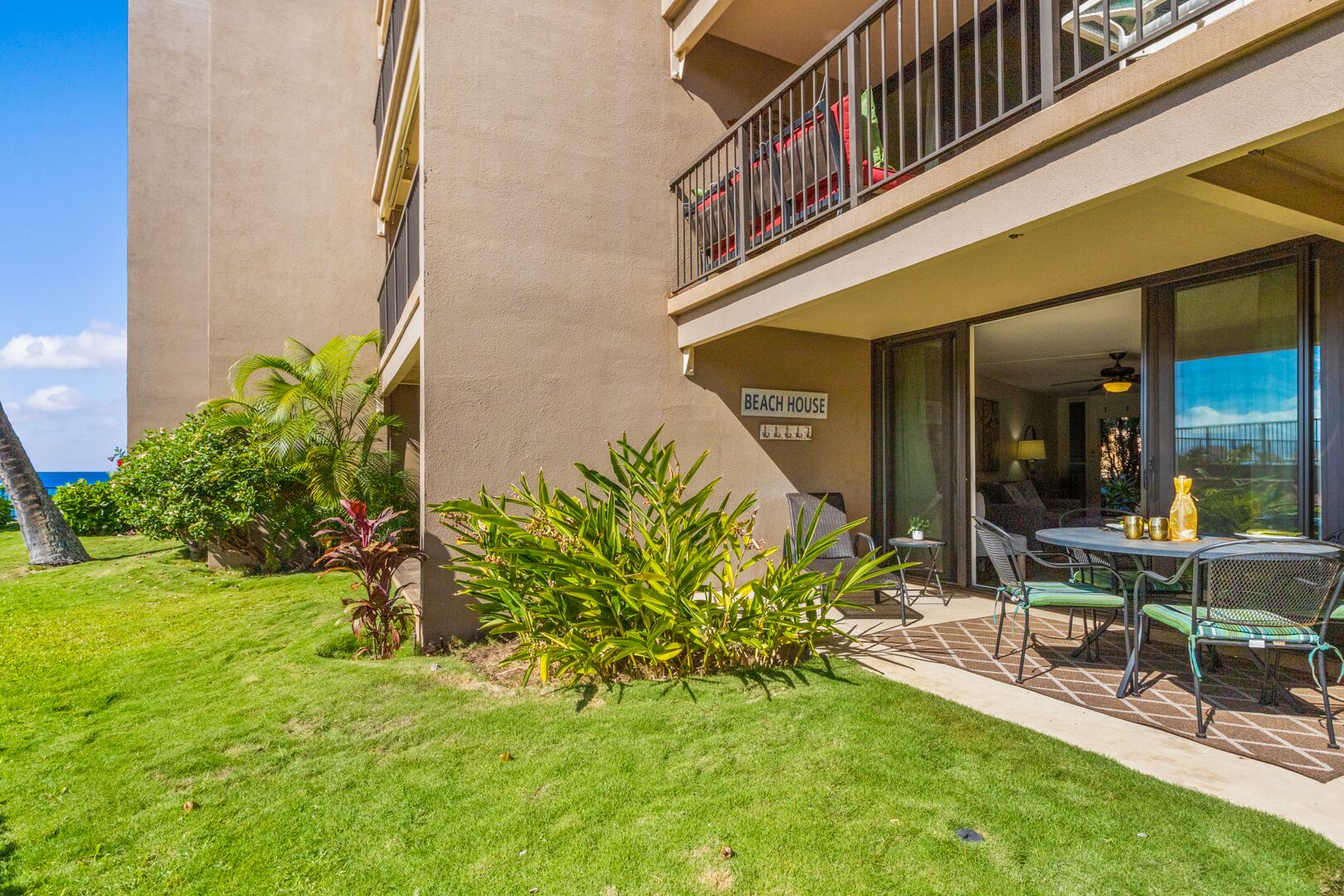 A hotel with a 'Beach House' sign, outdoor seating, and a well-maintained lawn.
