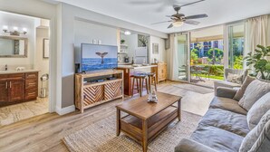 A spacious living room with a wooden coffee table, a sofa, and a TV displaying a whale tail. - Hale Ono Loa 106 - Relax Steps Away from the Ocean (Lahaina)