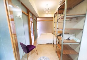 A compact bedroom with a bed, a purple chair, a wardrobe with shelves, and a chandelier. - Taipei 6BD Villa(Monthly Stay) (Taipei)