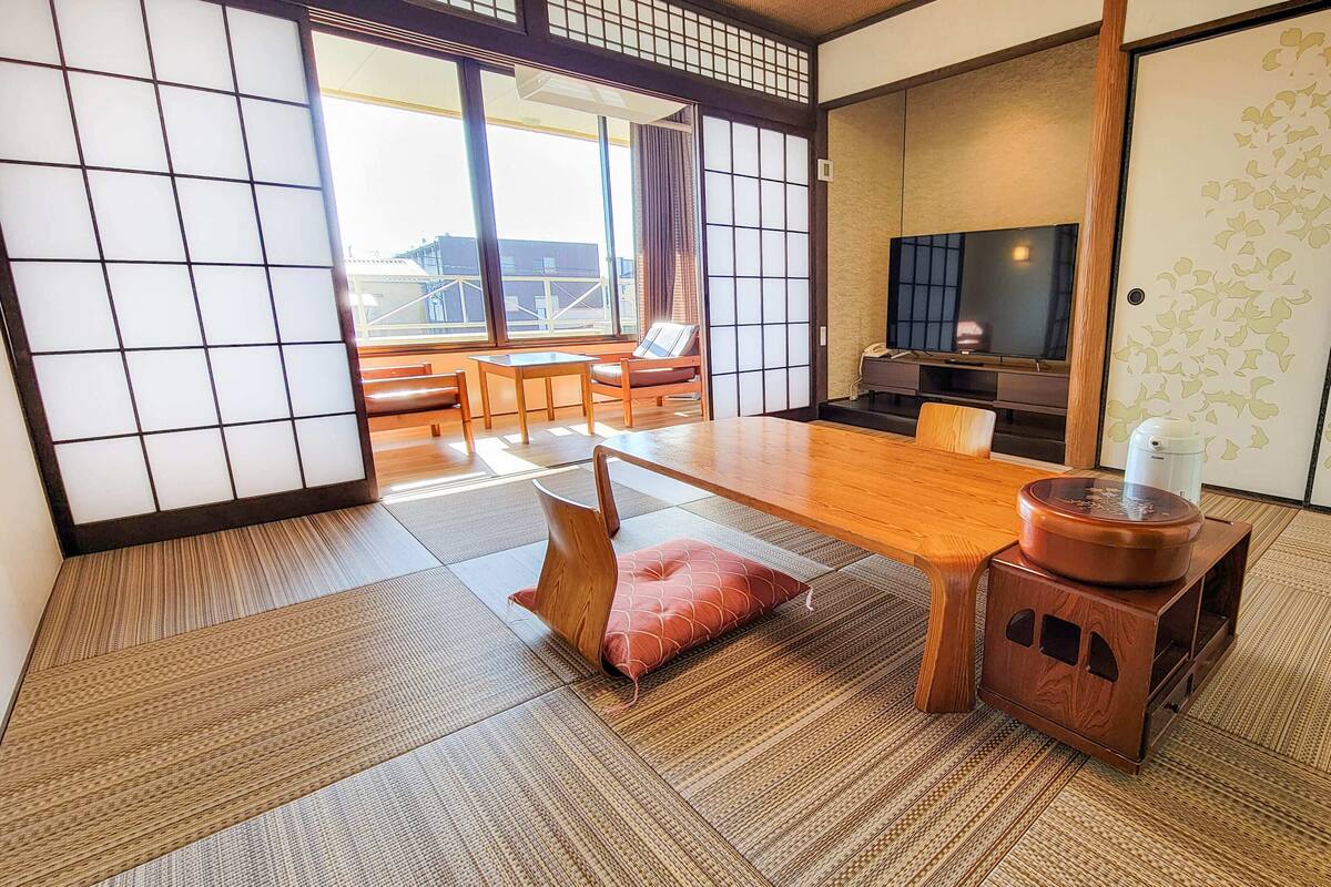 Una habitación japonesa tradicional con suelo de tatami, una mesa baja con cojín, televisor y puertas correderas.