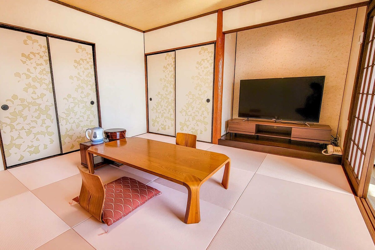 Une pièce de style japonais traditionnel, avec un sol recouvert de tatamis, une table en bois, un téléviseur et des portes coulissantes.