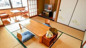 A tatami mat room with a low table, cushions, a television, and a traditional Japanese cabinet. - Aso Uchinomaki Onsen Daikanso (Aso)