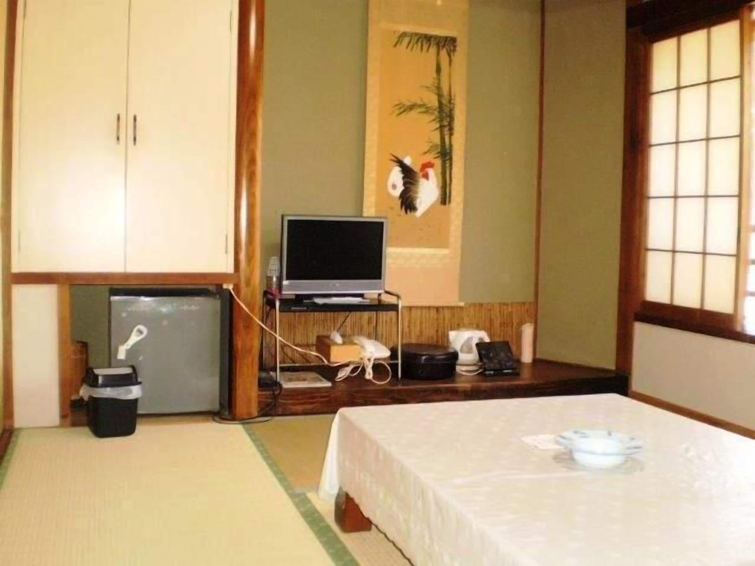 Una habitación japonesa tradicional con suelo de tatami, una cama, un televisor y un refrigerador pequeño.