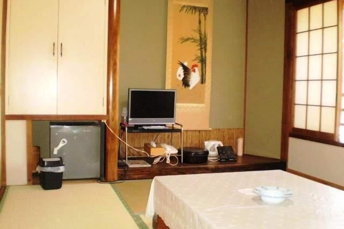 Une pièce de style japonais traditionnel, avec un sol recouvert de tatamis, un lit, une télévision et un petit réfrigérateur.