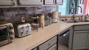 Une cuisine avec des meubles de couleur grise, un plan de travail sur lequel se trouve un grille-pain, un panier suspendu et des bocaux.