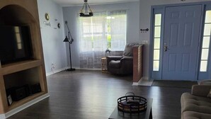 Un salon avec un parquet en bois foncé, un canapé gris, une table basse et un meuble pour la télévision.