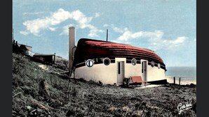 Una casa flotante con techo rojo, una chimenea y un pequeño porche con toldo a rayas rojas y blancas.