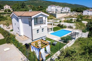 A two-story house with a swimming pool, a pergola, and a well-maintained lawn.